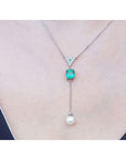 14K white gold necklace with triangle diamond cluster, cushion-cut emerald, and dangling white pearl.