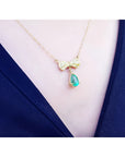 18K yellow gold bow-tie necklace with pave diamonds and a dangling pear-shaped emerald.