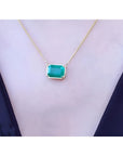 Emerald-cut Colombian emerald solitaire necklace in 18K yellow gold, worn on a black top.