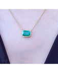 Emerald-cut Colombian emerald solitaire necklace in 18K yellow gold, on a black top, shown worn on a model's neck.