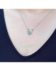 Emerald horseshoe pendant white gold and diamonds worn by a woman in a navy blue top.