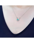 White gold oval emerald horseshoe necklace with diamonds, worn on a person.