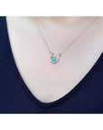 White gold oval emerald horseshoe necklace with diamonds, worn on a person.