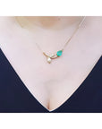 14K yellow gold twig necklace with a pear-cut natural emerald and diamond leaves on a woman's neck.