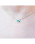 Oval Muzo emerald necklace with diamond halo on a delicate 14K yellow gold chain.