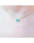 Oval Muzo emerald necklace with diamond halo on a delicate 14K yellow gold chain.
