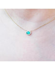 Oval Muzo emerald necklace with diamond halo on a delicate 14K yellow gold chain.