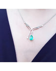 14K white gold necklace with a pear-shaped emerald and diamond chevron pendant on a woman's neck.