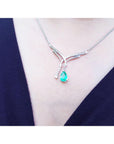 A teardrop emerald necklace with a green teardrop pendant on a person wearing a dark blue top.