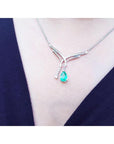 A teardrop emerald necklace with a green teardrop pendant on a person wearing a dark blue top.