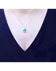 Tilted heart emerald necklace with halo diamonds on an 18K gold chain, worn on a woman's neck.
