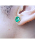 Round bluish-green Colombian emerald stud earring in 14K yellow gold prong setting on an ear.