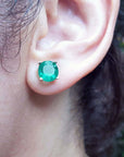 Close-up of an ear wearing a genuine emerald stud earring with a blurred natural background