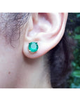 Round bluish-green Colombian emerald stud earring in 14K yellow gold, worn on an ear.