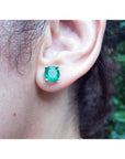 Round bluish-green Colombian emerald stud earring in 14K yellow gold, worn on an ear.