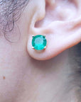Close-up of an ear wearing a round cut emerald stud earring.