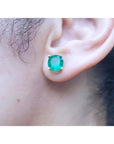 Close-up of an ear wearing a round cut colombian emerald stud earring.