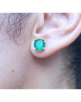 Close-up of an ear wearing a round cut colombian emerald stud earring.