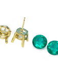 Gold earring posts with round cut loose natural emeralds aside on a white background