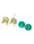 Gold earring posts with round cut loose natural emeralds aside on a white background