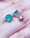 Front and side position displaying a pair of round cut emerald earrings on a hand