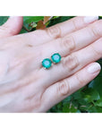 Round bluish-green Colombian emerald stud earrings in 14K yellow gold on a hand.