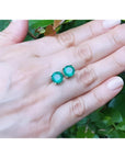 Round bluish-green Colombian emerald stud earrings in 14K yellow gold on a hand.
