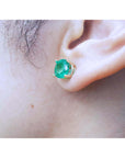 Close-up of an ear wearing a round cut emerald stud earring, to show left ide profile
