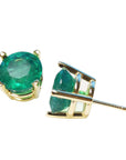 Underside view of a pair of yellow gold natural emerald stud earrings on a white background