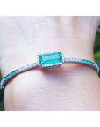 Close-up of a bracelet with a natural emerald gemstone on a wrist against a blurred natural background