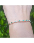 Flexible 14K yellow gold bangle with round emeralds and accent diamonds on a wrist.