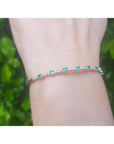 Flexible 14K yellow gold bangle with round emeralds and accent diamonds on a wrist.