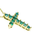 A 14k yellow gold cross necklace pendant with natural colombian emeralds on a side profile view.