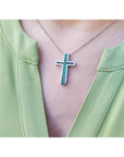 Cross-shaped necklace with genuine colombian emeralds worn by a person in a green top.