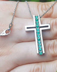 White gold cross pendant necklace with round emeralds held in a hand.
