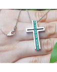 White gold cross pendant necklace with round emeralds held in a hand.