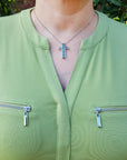 A woman wearing a green jacket with zippers and an emerald cross necklace outdoors.