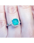 1.71 ct. Colombian emerald cushion-cut halo diamond ring in 14K white gold on a finger.