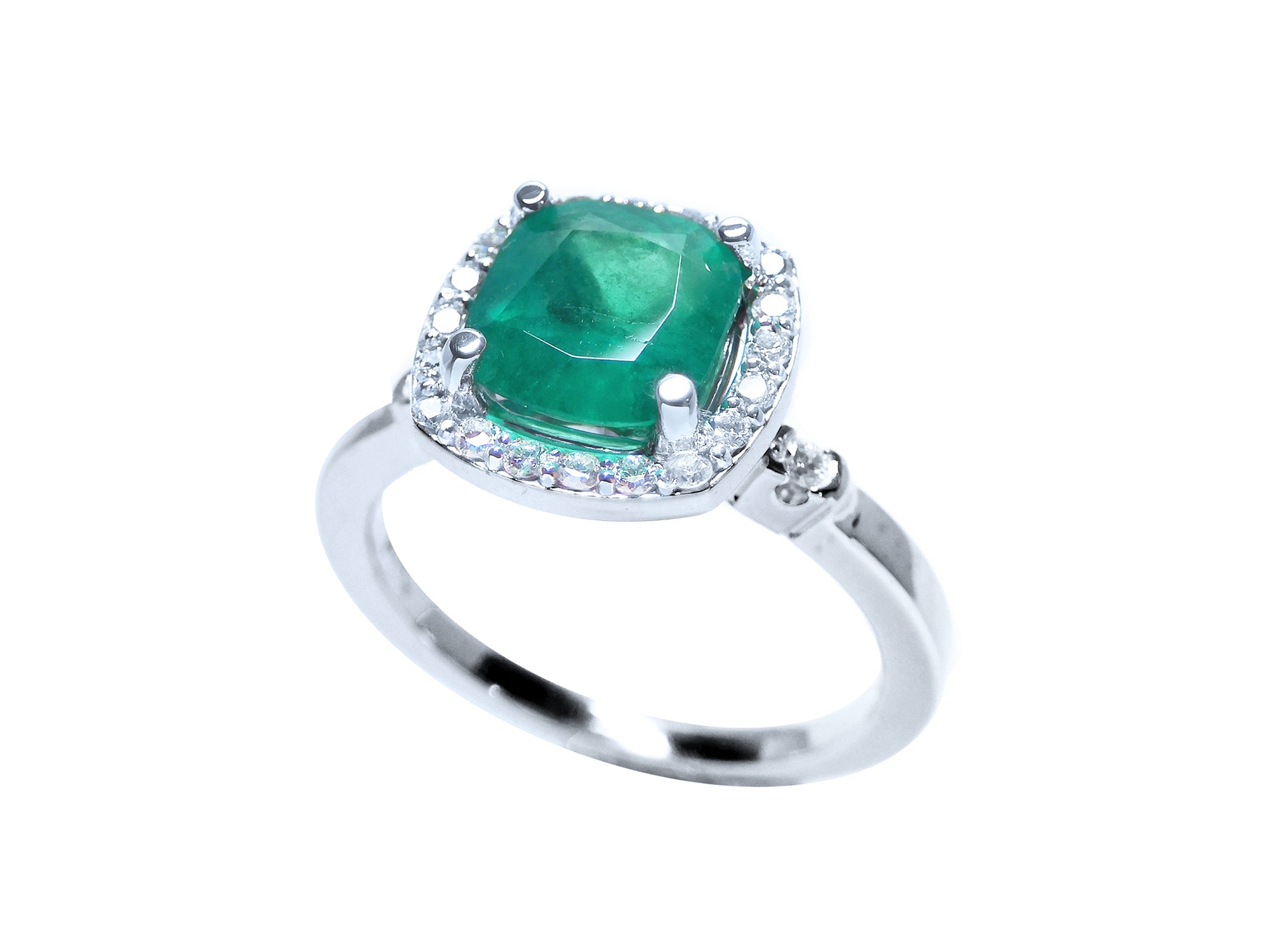 A 14k white gold ring with a cushion cut natural Colombian emerald encircled by a halo diamond on a white background