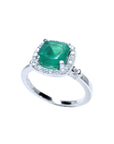 A 14k white gold ring with a cushion cut natural Colombian emerald encircled by a halo diamond on a white background