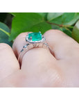 1.71 ct. Colombian emerald cushion cut halo diamond ring in 14K white gold on a finger.