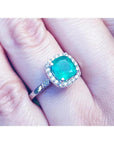 A natural Colombian emerald cushion cut with a halo diamond in white gold on a finger.