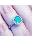 A natural Colombian emerald cushion cut with a halo diamond in white gold on a finger.