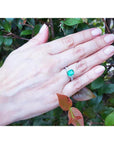 Hand wearing an emerald ring with a natural background.