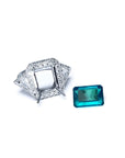 18K white gold diamond halo ring setting with trillion sides next to a loose rectangular emerald.