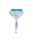 18K white gold ring with a rectangular emerald center stone, surrounded by diamonds and trillion cut sides.