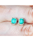 Emerald green gemstone earrings held between fingers.