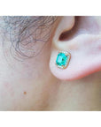 Colombian emerald halo stud earring with diamonds in 14k yellow gold on an ear.