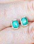 Emerald green gemstone earrings placed between fingers.