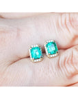 Emerald green gemstone earrings placed between fingers.